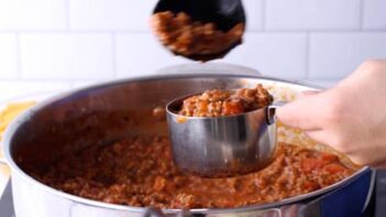 A spoon scooping out red sauce into a measuring cup to set aside for later.