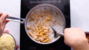 Stirring cooked penne pasta with a spoon in boiling water.