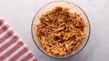 A bowl with ziti pasta coated with a creamy red beefy sauce.