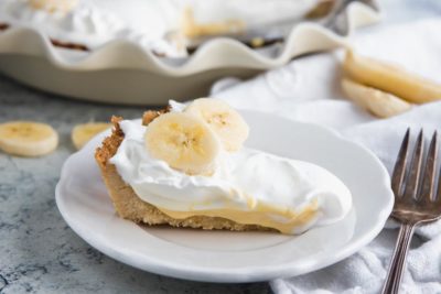 a slice of keto banana cream pie on a plate with a whole pie in the background