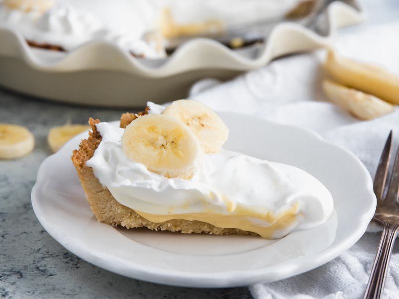 a slice of keto banana cream pie on a plate with a whole pie in the background