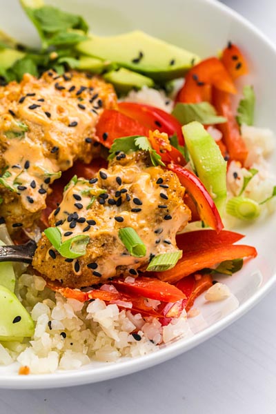 Keto bang bang chicken covered in spicy sauce and topped with black sesame seeds and green onions.