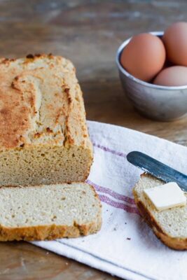 a slice of bread from egg loaf sits in front of the whole loaf with a bowl of eggs next to it