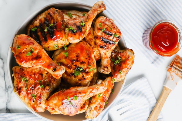 looking down on a plate of saucy bbq chicken with a side of bbq sauce and a basting brush