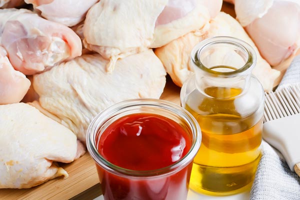 raw chicken on a baking tray with bbq sauce and olive oil in front