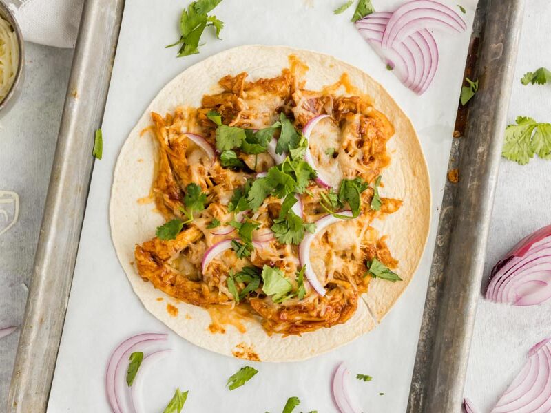 tostada topped with cilantro and red onion on a parchment lined tray with sliced red onion around