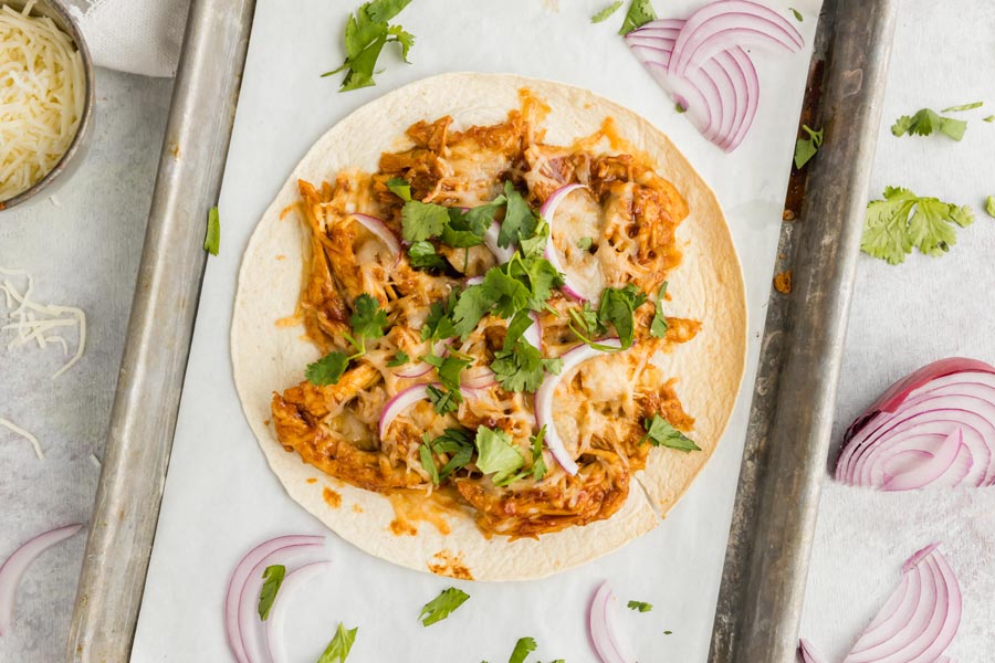 tostada topped with cilantro and red onion on a parchment lined tray with sliced red onion around