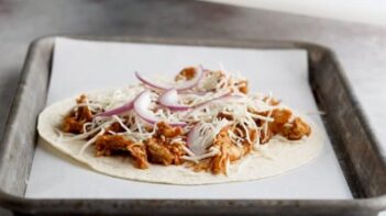 a tortilla with chicken, shredded cheese and onion on top