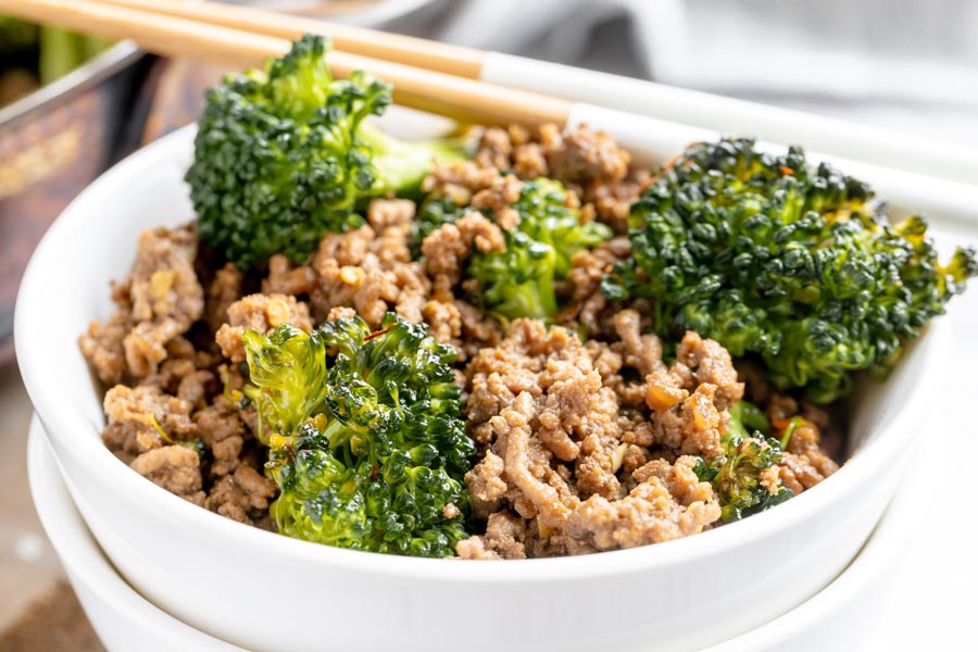 a bowl of broccoli beef with chopsticks near