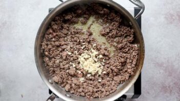 a skillet with browned ground beef and a bunch of minced garlic in the center