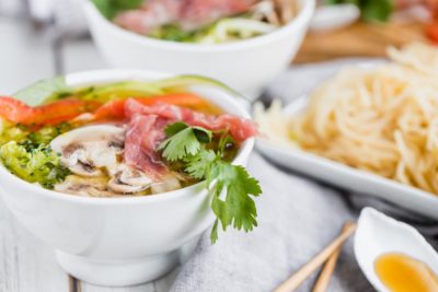 cilantro hanging down off a bowl of pho with vegetables and beef on top