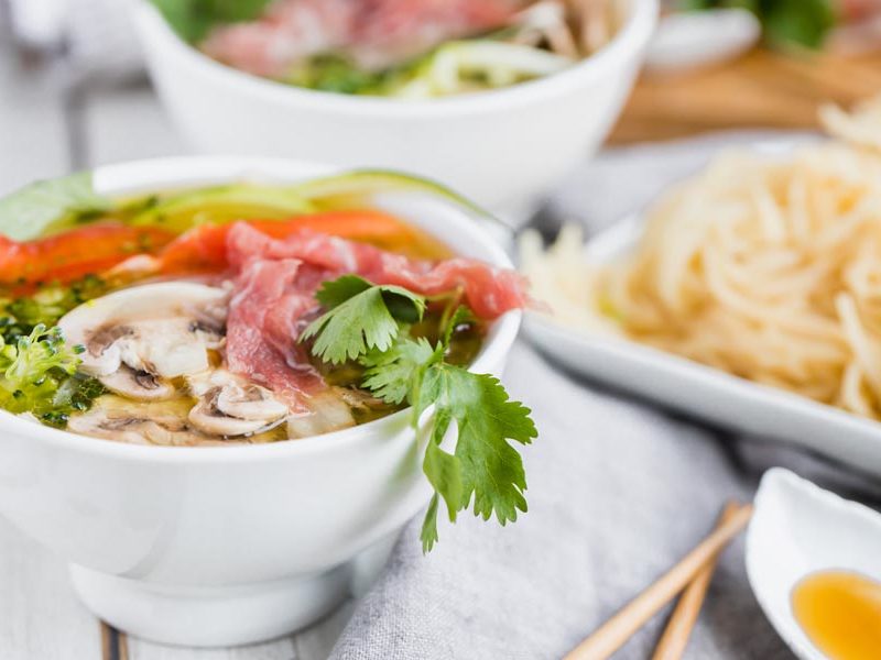 cilantro hanging down off a bowl of pho with vegetables and beef on top