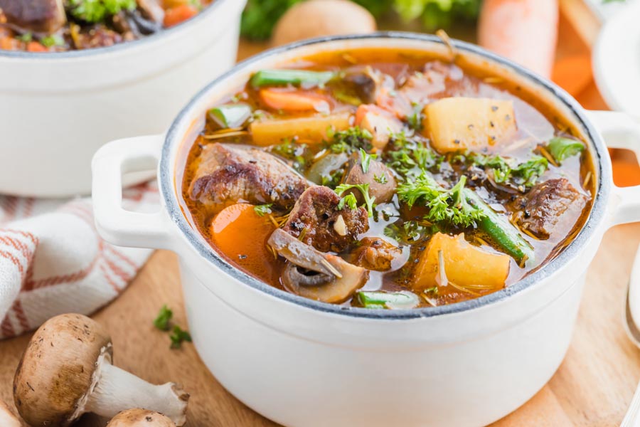 A hearty bowl of beef stew with parsley, green beans, carrots and mushrooms in a tomato broth.