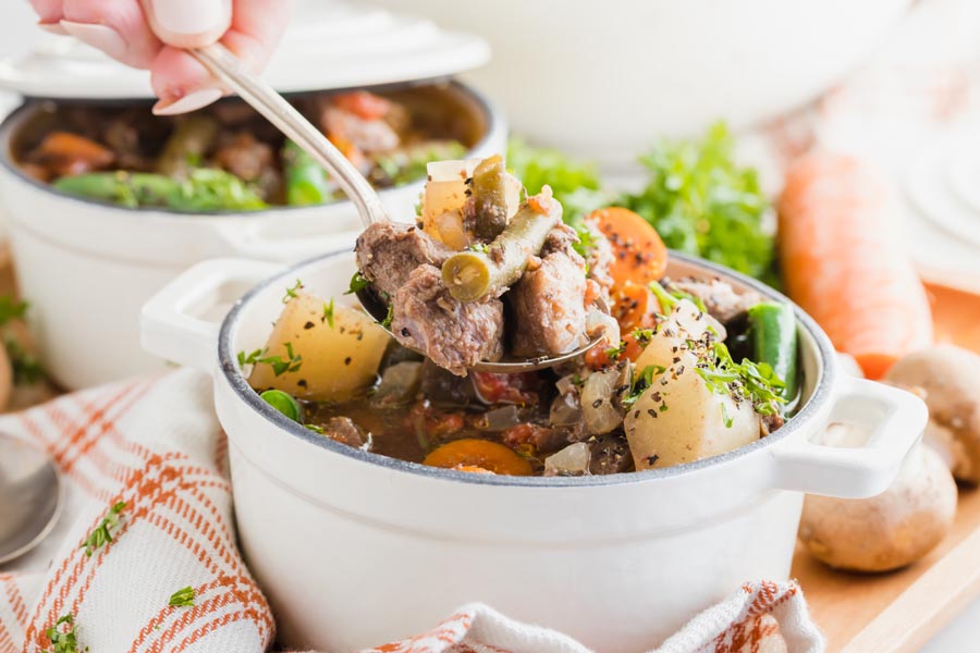 a hand holding a spoonful of beef stew with chunks of beef and green beans in it.