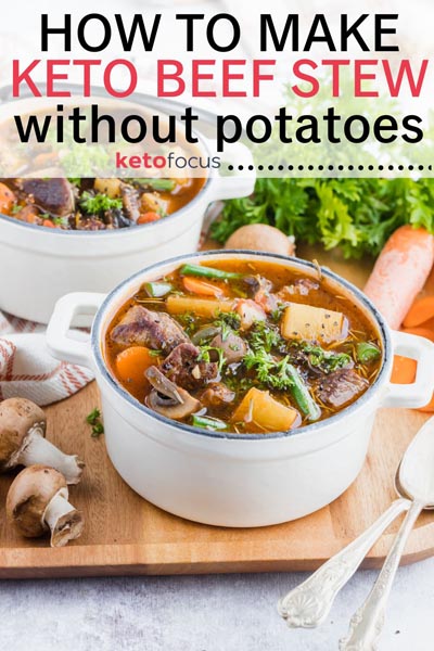 A cream colored pot filled with soup with mushrooms, daikon radish, beef, carrot and green beans inside. Spoons rest off to the side along with carrot and mushroom.