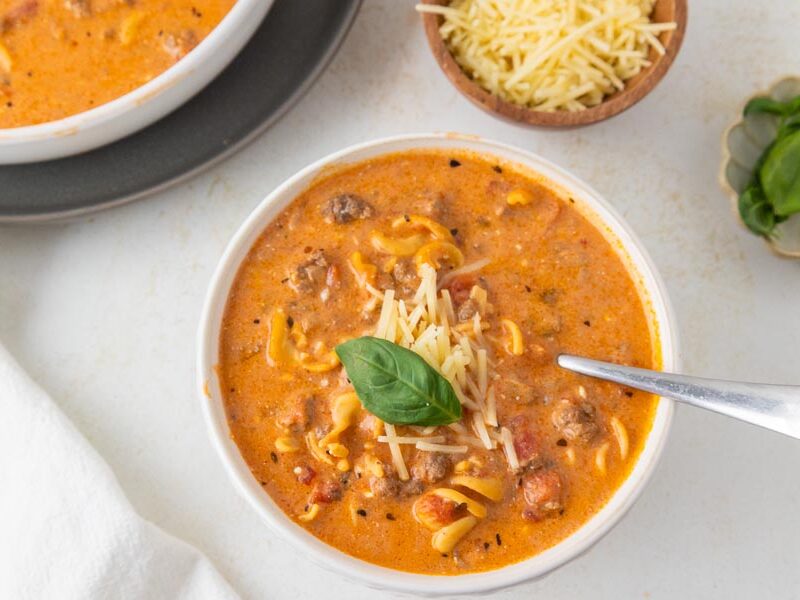A spoon sitting in a bowl of creamy tomato soup topped with parmesan cheese and basil.