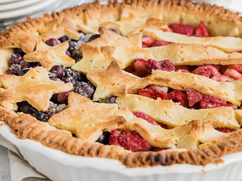 a side view of a pie filled with blueberries and raspberries and decorated with lattice that looks like American Flag