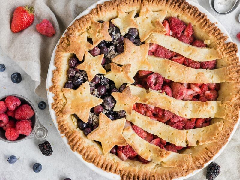 a keto pie decorated like an American Flag with blueberries, strawberries, raspberries and blackberries scattered around