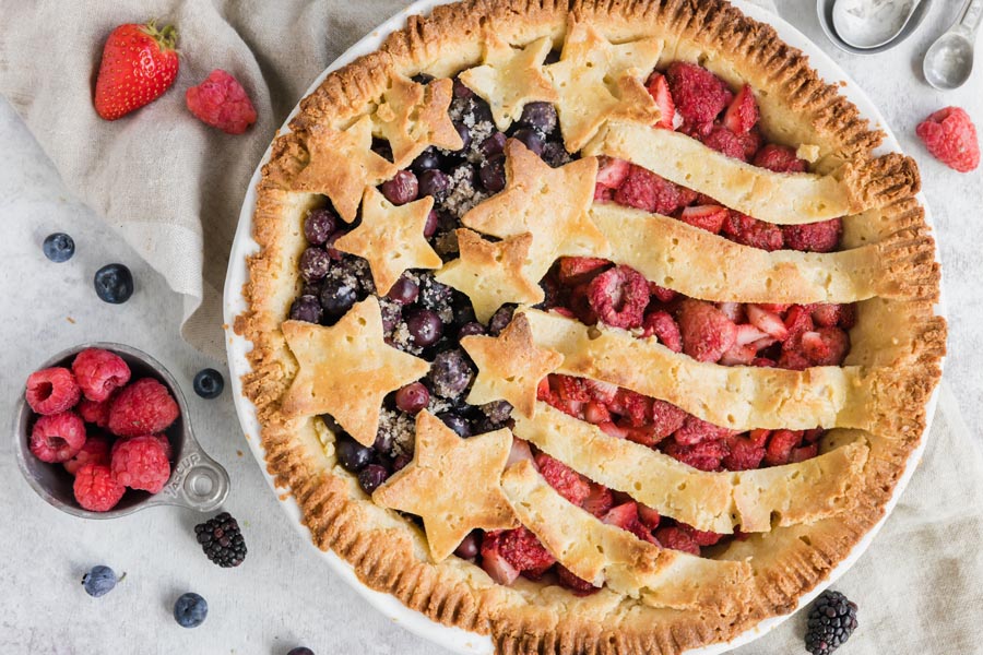 a keto pie decorated like an American Flag with blueberries, strawberries, raspberries and blackberries scattered around