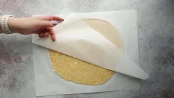 peeling the top layer of parchment paper off to reveal pie crust