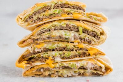 Four crunchwraps stacked on each other filled with Big mac components like burger patties, cheese, lettuce, onion and pickles.