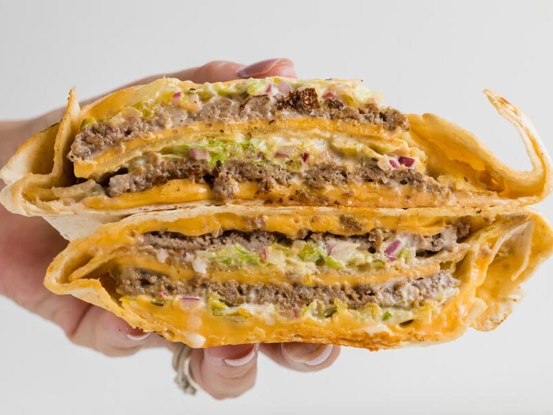 Hand holding a sliced Big Mac-style crunchwrap with beef, cheese, lettuce and onion.