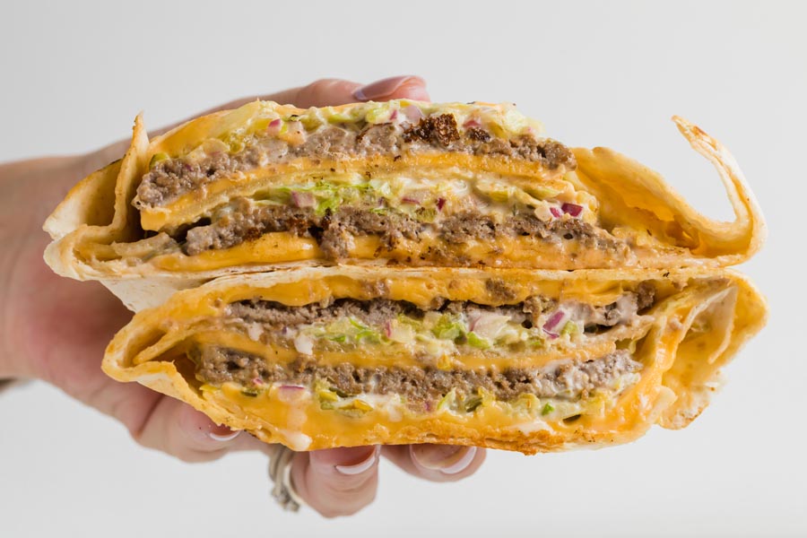 A hand holding a big mac wrap cut in half. Inside are layers of burger, melted cheese, lettuce and onion.