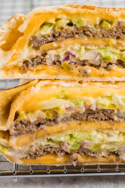Two thick burgers wrapped in a tortilla stacked on each other on a wire rack.