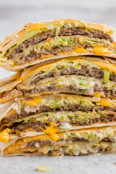 A big stack of burger wraps filled with shredded lettuce, hamburger patties and American cheese dripping down.