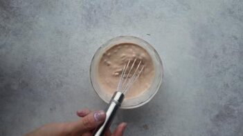 A hand whisking thousand island dressing in a small bowl.