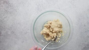 A hand stirring tortilla dough with a spoon.