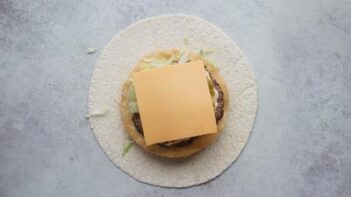 Assembling a wrap filled with a burger cheese and lettuce.