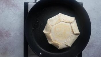 A sealed crunchwrap frying in a non-stick skillet.
