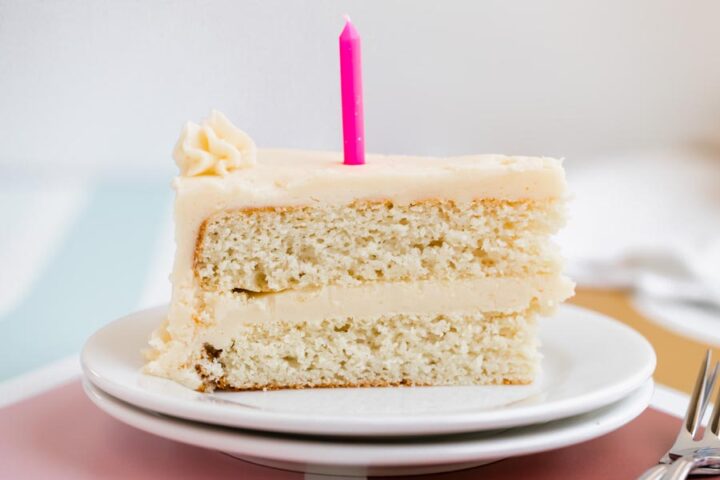 Side view of a slice of keto white cake showing the moist crumb and thick layer of frosting, topped with a single pink candle.