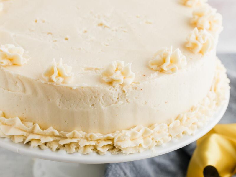 Frosted keto vanilla birthday cake decorated with piped buttercream swirls on the edges.