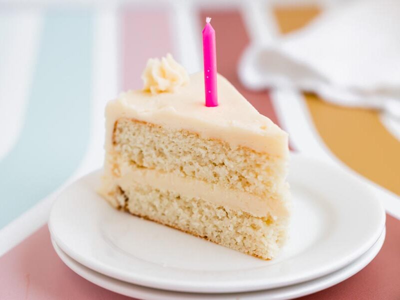 A bright and colorful view of a slice of keto vanilla cake with a pink candle and piped frosting on top.