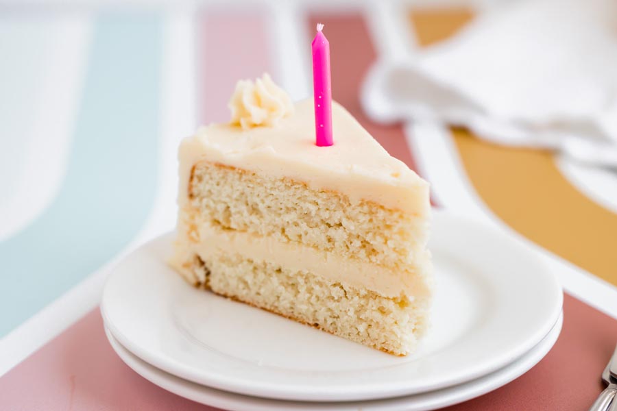 A bright and colorful view of a slice of keto vanilla cake with a pink candle and piped frosting on top.