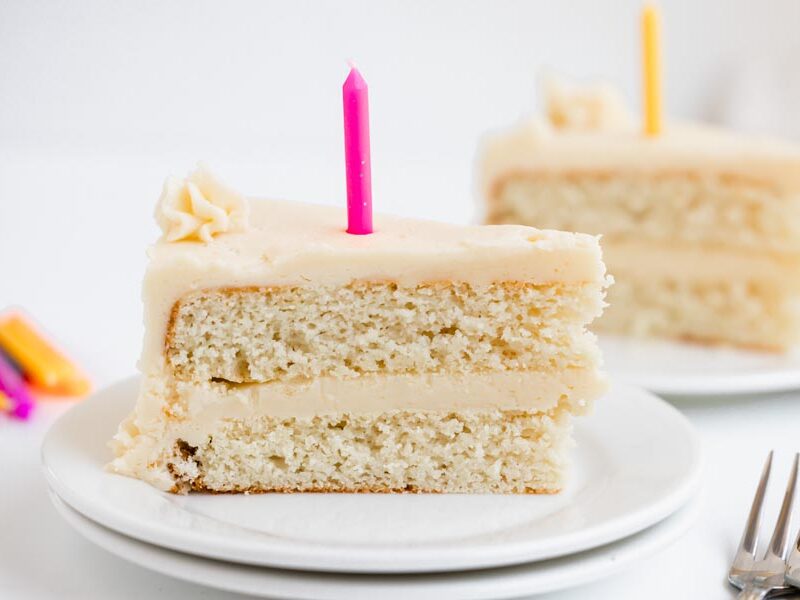 Two slices of keto white birthday cake on plates, each topped with a brightly colored candle.