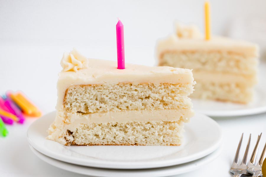 Two slices of keto white birthday cake on plates, each topped with a brightly colored candle.