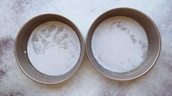 Two 8-inch round cake pans lined with parchment paper and lightly greased, ready for cake batter.