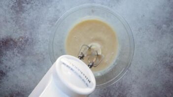 Wet ingredients being mixed with an electric hand mixer to form a smooth batter.