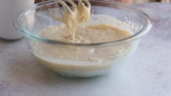 Finished keto cake batter dripping from mixer beaters into a glass bowl.