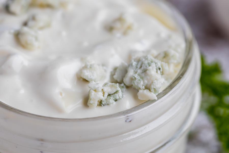 blue cheese sits on top of creamy mayo based dressing in a clear jar