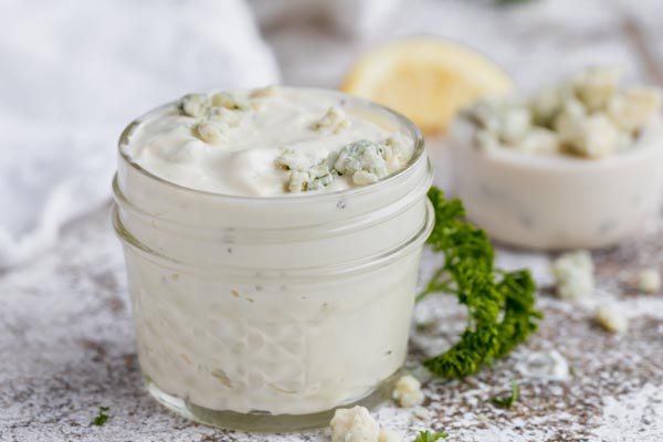 a small mason jar filled with a creamy blue cheese dressing next to parsley sprigs