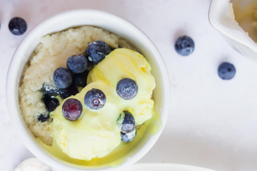 looking down onto a mug with blueberry shortcake in it topped with blueberries and ice cream