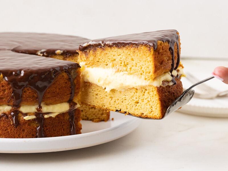 Slice of keto Boston cream pie with two cake layers, custard filling and chocolate ganache.