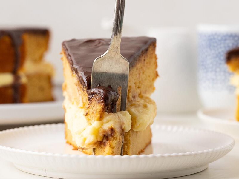 Fork cutting into a slice of keto Boston cream pie, revealing fluffy cake, creamy custard filling, and smooth chocolate topping.