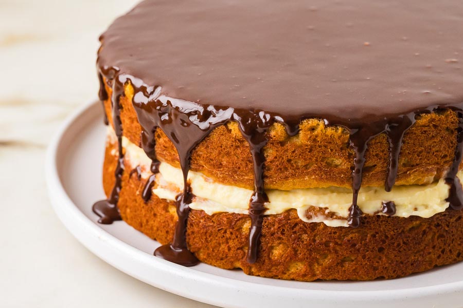 Whole keto Boston cream pie layered with vanilla custard and topped with a thick chocolate ganache that drips down the sides.