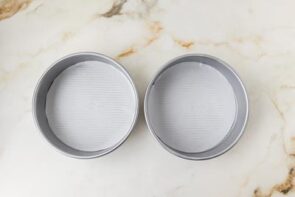 Two round cake pans lined with parchment paper, prepared for baking the keto Boston cream pie cake layers.