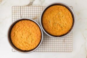 Two baked keto cake layers cooling in round cake pans on a wire rack.